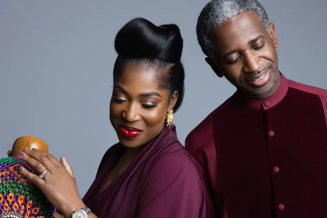 Couple in deep red outfits standing back to back with a beaded instrument